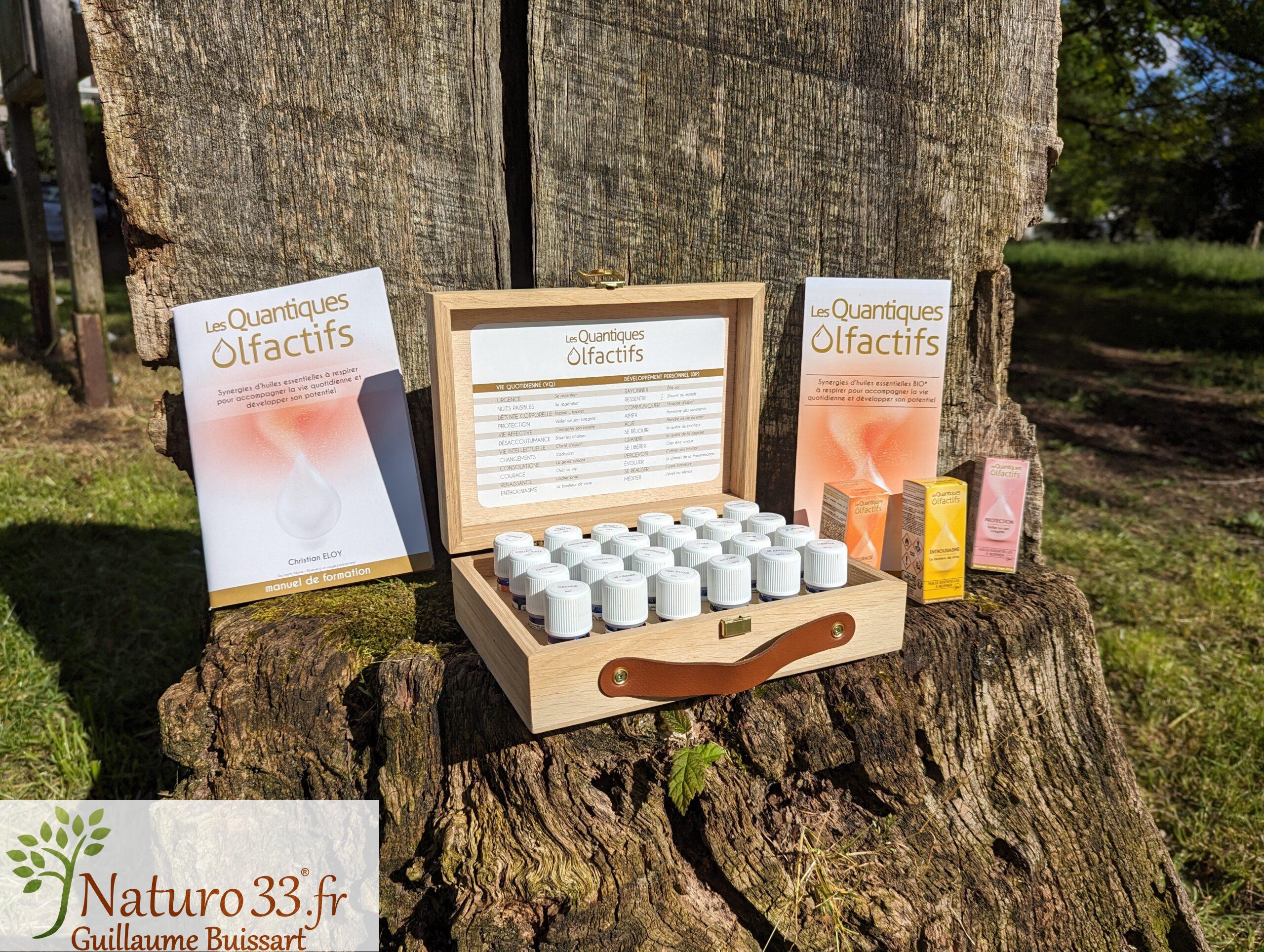 Coffret de 24 synergies d'huiles essentielles Quantiques Olfactifs posés sur une souche de bois dans un jardin